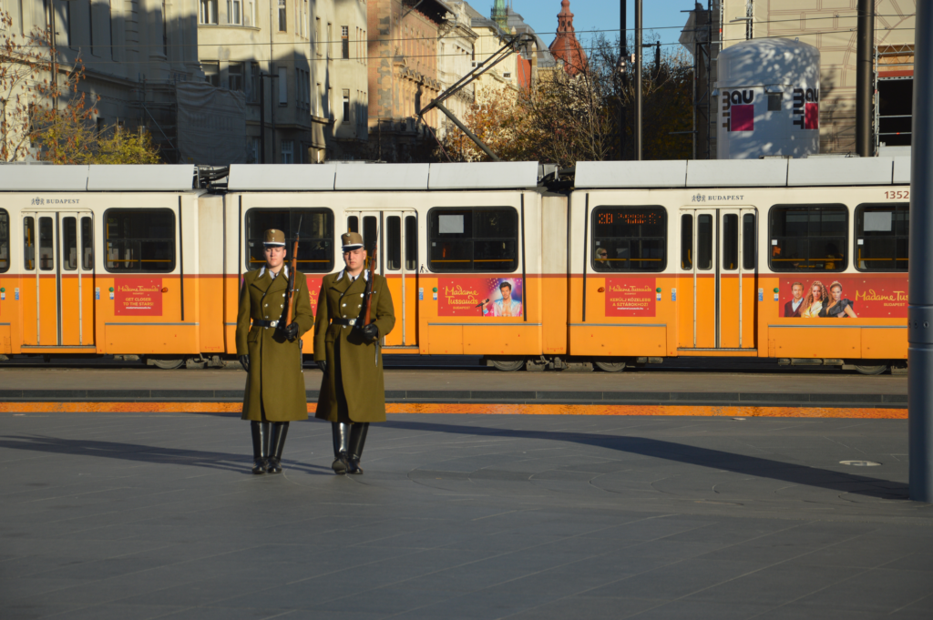 Soldiers march through the streets of Hungary next to the parliament building as a tram passes by.