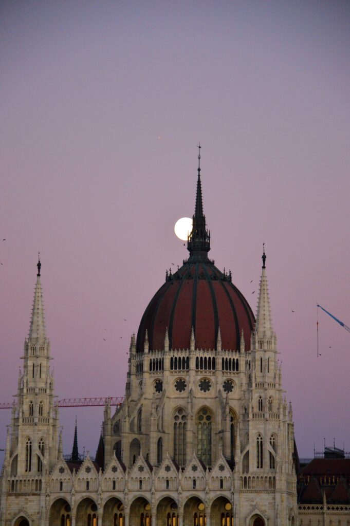 Moon halfway visible through the government parliament in Budapest.